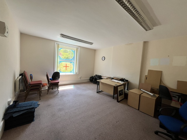 Large office room with a double-height window with stained-glass effect and stored office furniture.