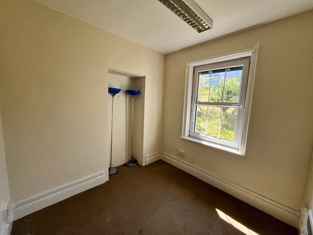 Small office room with a window providing natural light and a recessed alcove containing two floor lamps.