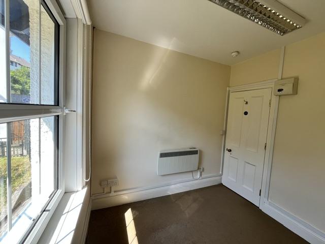 A small office with a large window, electric wall heater, cream-coloured walls and natural daylight.