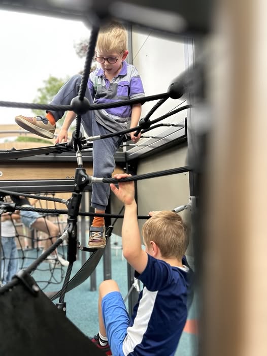 Children climbing and playing on rope equipment in an outdoor playground.
